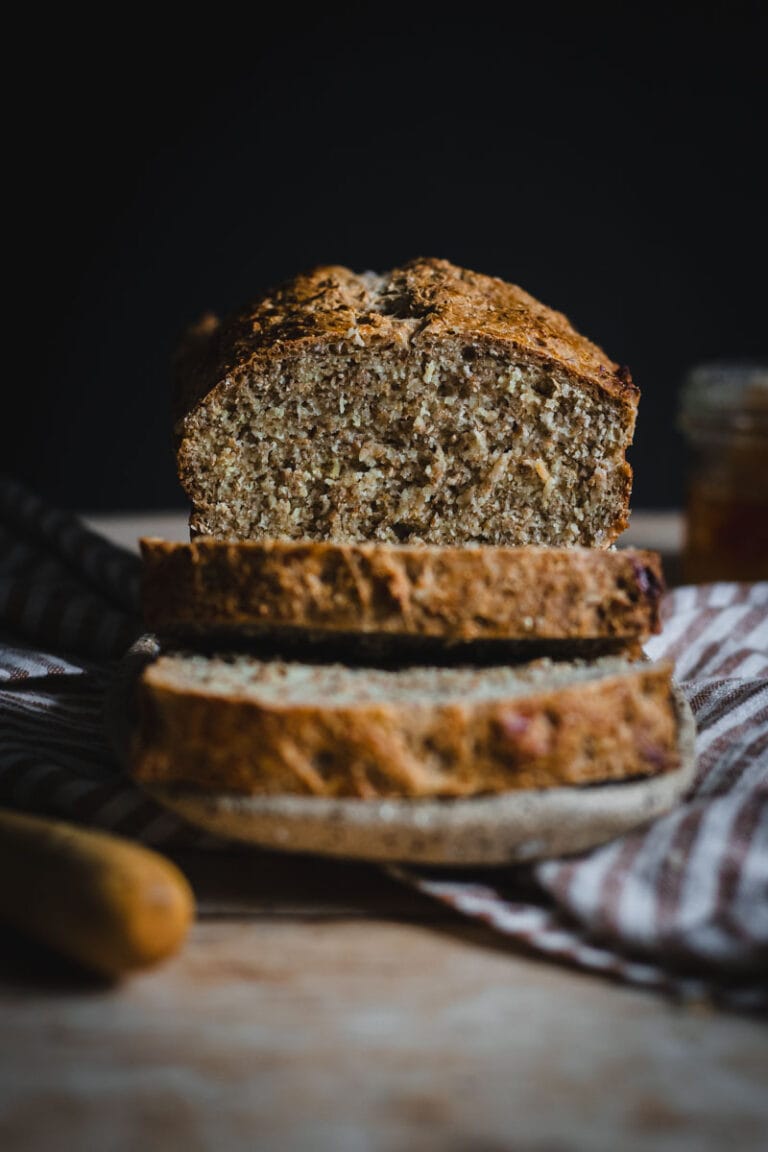 The finished loaf of Irish Brown Bread with two slices cut laying on their side on the plate. A small jar of honeycomb and a knife sit beside the loaf.