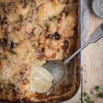 A cream enamel cast iron roasting pan full of cheesy potato bake. A spoonful has been eaten out of the corner.