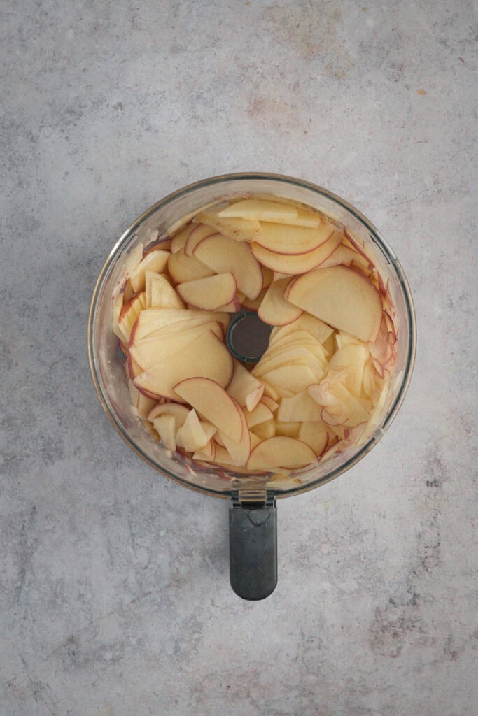 A food processor bowl full of sliced potatoes. 