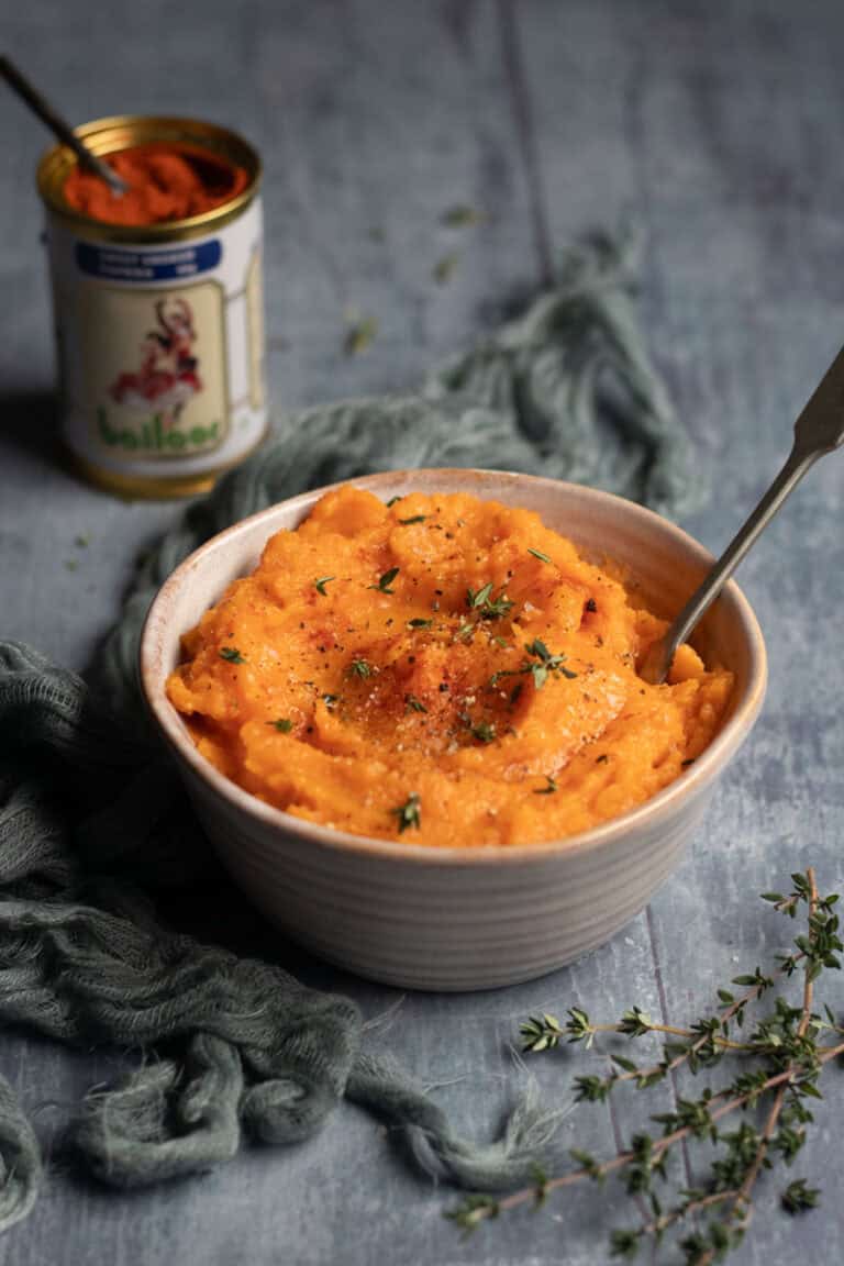 A bowl of sweet potato mash with a spoon in it. A tin of sweet smoked paprika sits in the background.
