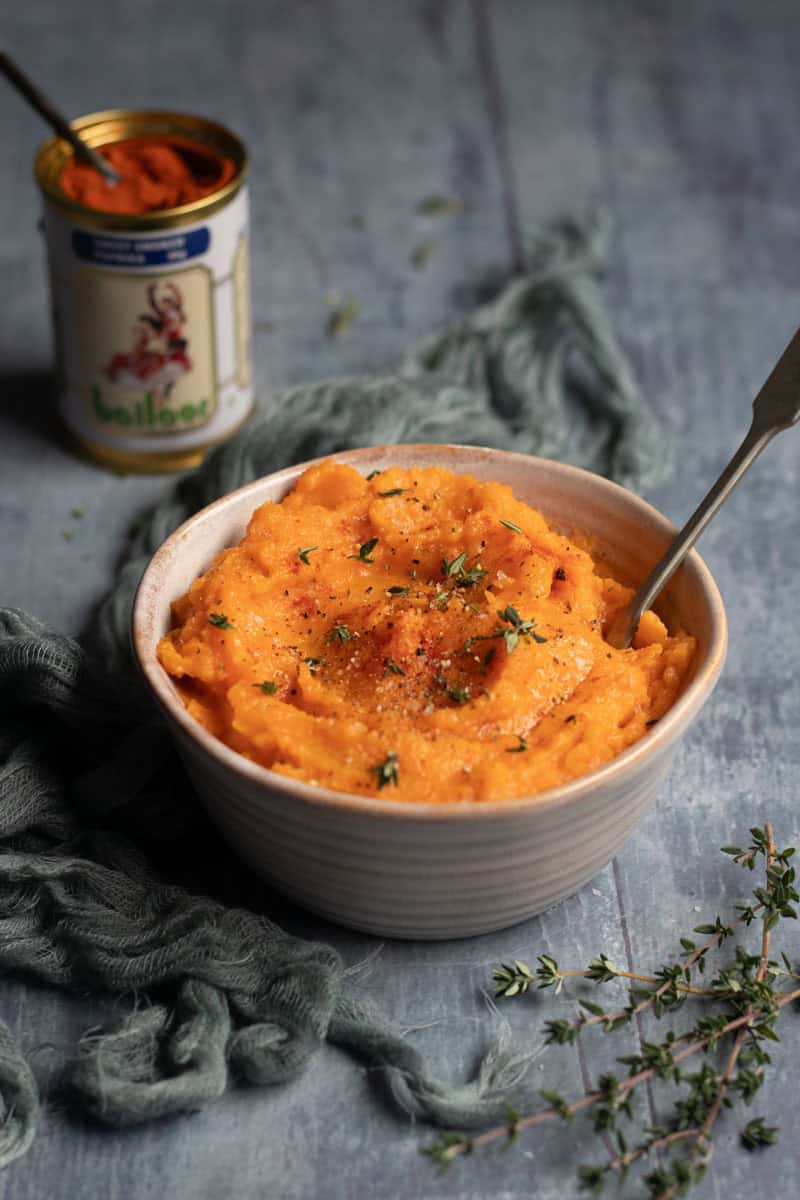 A bowl of sweet potato mash with a spoon in it. A tin of sweet smoked paprika sits in the background.