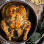 Roasted chicken in a Dutch oven with potatoes and herbs.